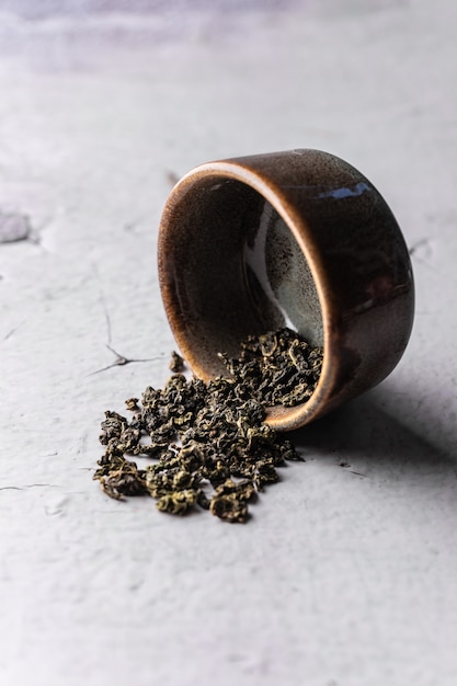 Selective focus natural green leaf tea brewing in a clay bowl vertical angle macro on a light backgr...