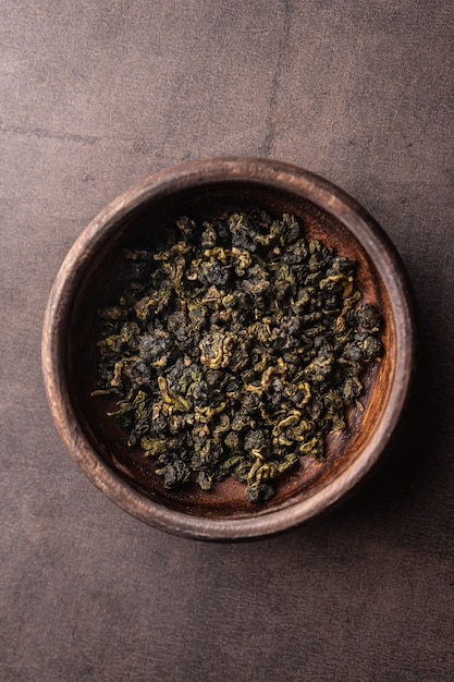 Selective focus natural green leaf tea brewing in a wood bowl vertical angle macro on a dark backgro...