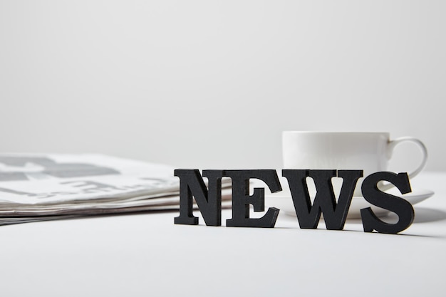 Selective focus of news lettering near cup glasses and newspaper on white