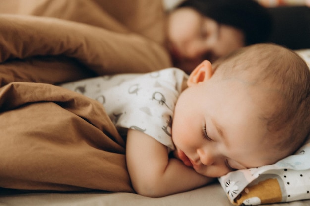 Selective focus noise effect portrait of a baby who fell asleep during the day on a bed next to his mother