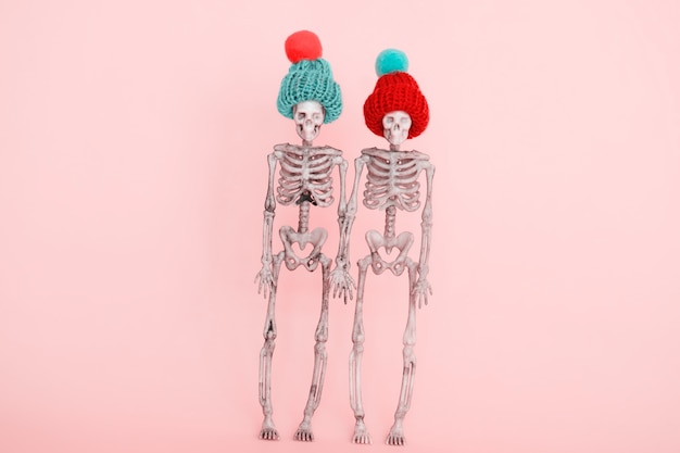 Photo selective focus pair of skeletons wearing cute knitted hat on a pink background