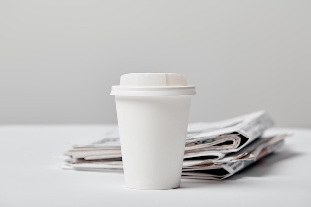 Selective focus of paper cup with drink near newspapers on grey