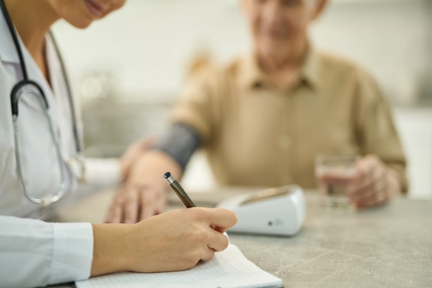 Selective focus photo of busy doctor taking notes in medical history of a senior citizen