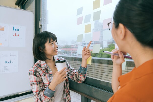 写真 ガラス窓の壁で会議をしているときに上司と話している付箋紙を指している幸せな女性サラリーマンのセレクティブ フォーカス写真。