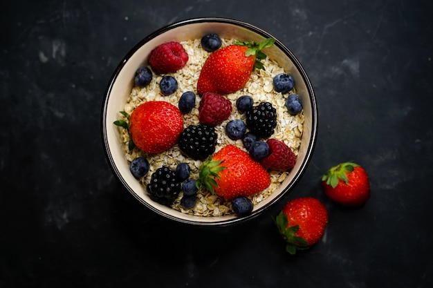 Messa a fuoco selettiva, corretta alimentazione, colazione sana, piastra profonda con cereali, farina d'avena, fragole fresche, lamponi, mirtilli e more