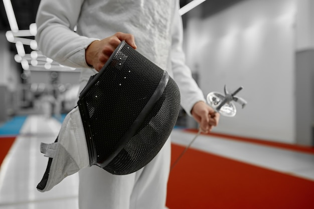 Selective focus on protective fencing mask in hand of young fencer