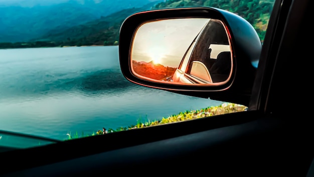 Выборочный фокус Зеркало заднего вида автомобиля, отражающее закат. Закат в зеркале заднего вида. Красивое озеро и отражение заката через боковые зеркала автомобиля. Идея концепции дорожного путешествия
