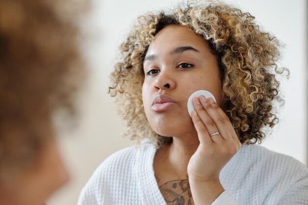 Selective focus on reflection in mirror of young woman taking care of her face