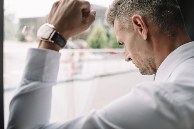 Photo selective focus of sad businessman standing with clenched fist near window