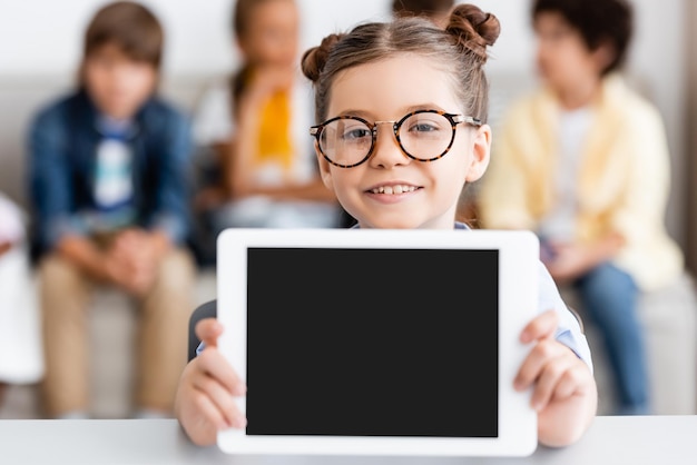 Photo selective focus of schoolgirl in eyeglasses holding digital tablet at desk