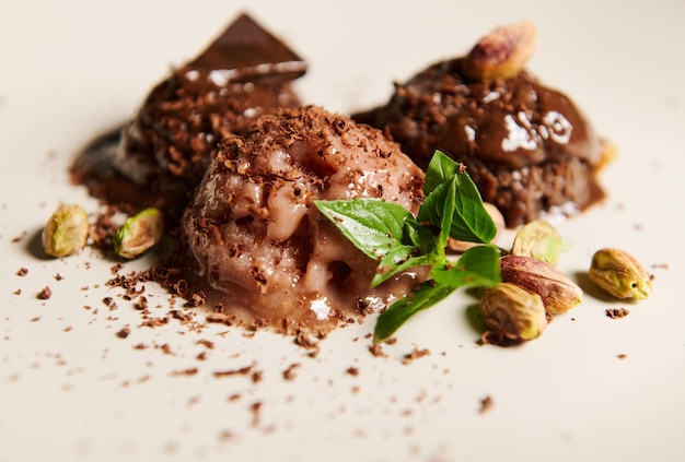 Selective focus on scoops of chocolate ice cream topped with pistachio and lemon basil leaves melting on a white plate