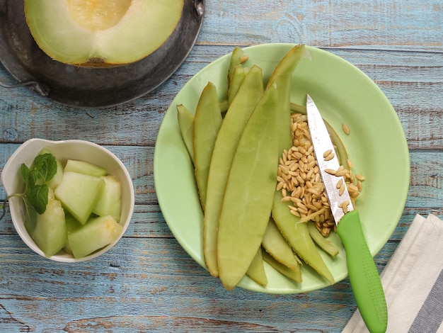 Selective focus of seeds and melon peel in green plate with the knife on blue wooden rustic table