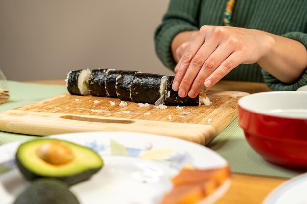 Photo selective focus shot of a cook cutting sushi on cutting board with various ingredients on a table