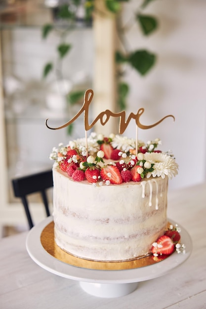 Photo selective focus shot of delicious white wedding cake with red berries, flowers and cake topper