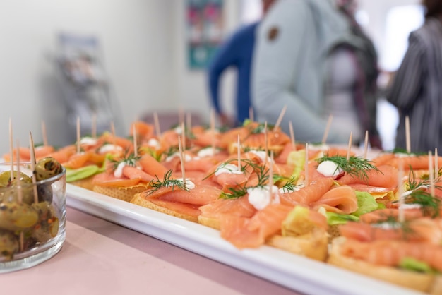 Selective focus shot of a fourchette table with salmon canapes on the background of guests