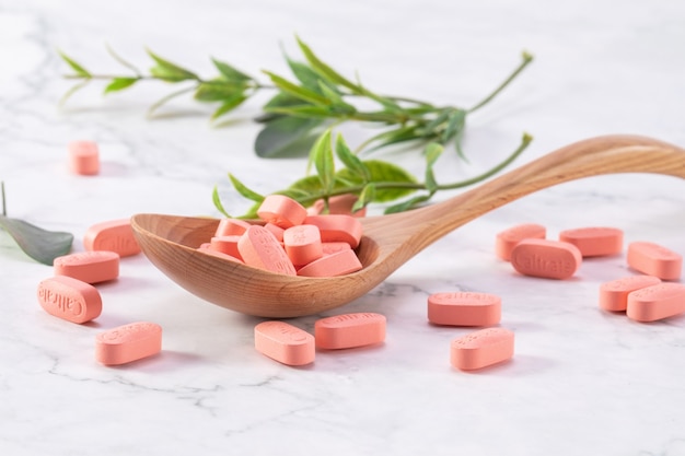 Selective focus shot of medical pills on a wooden spoon with green leaves