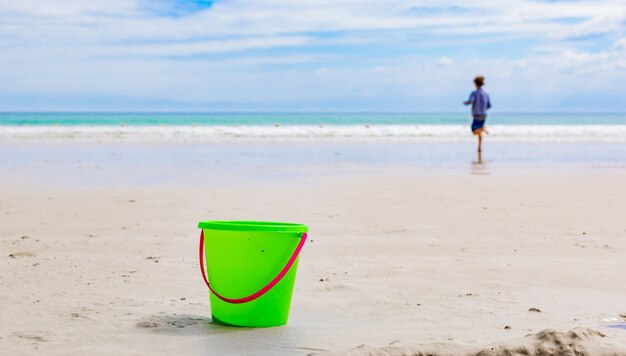 Selective focus shot of a sand bucket on a beach and a boy running towards the sea in Cape Town