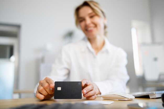 Foto messa a fuoco selettiva della donna di affari sorridente che tiene la carta di credito