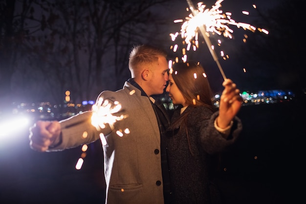 Selective focus of sparklers in hands of young couple enjoying holiday time outdoors.