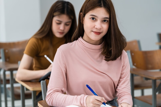 教室の講義椅子に座っている10代の大学生の選択的な焦点は、最終試験テストを行う際に試験紙の解答用紙に書き込みます。学生服を着た女子学生。