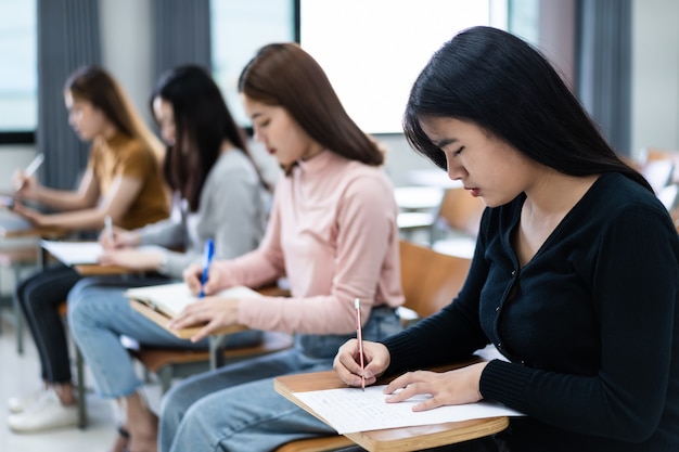 教室の講義椅子に座っている10代の大学生の選択的な焦点は、最終試験テストを行う際に試験紙の解答用紙に書き込みます。学生服を着た女子学生。