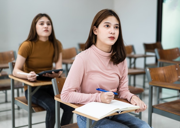 Selective focus of the teen college students sitting on lecture
chair in classroom write on examination paper answer sheet in doing
the final examination test. female students in the student
uniform.