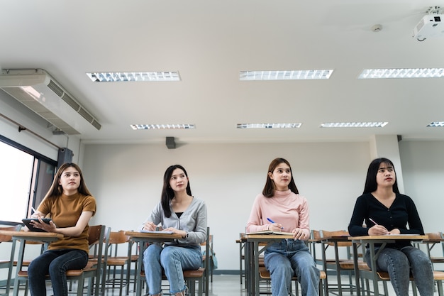 Selective focus of the teen college students sitting on lecture\
chair in classroom write on examination paper answer sheet in doing\
the final examination test. female students in the student\
uniform.