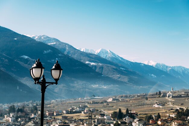 Selective focus of traditional lamppost and dining set table overlooking Sondrio an Italian town and comune located in the heart of the wineproducing Valtellina region