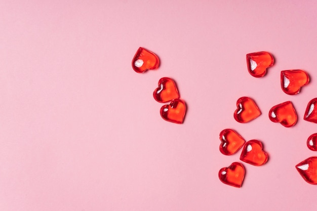 Selective focus. Valentine's day card. glass red hearts scattered on a pink background. the view from the top. copyspace