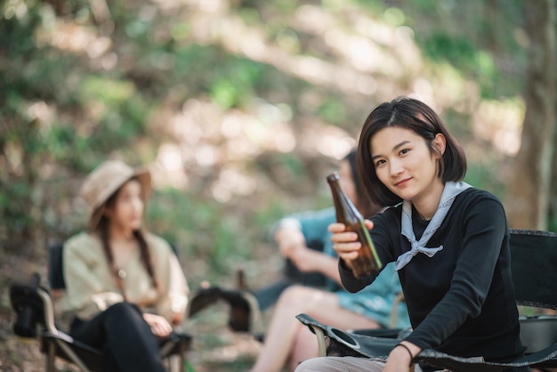 Messa a fuoco selettiva giovane bella donna asiatica e la sua ragazza seduta davanti alla tenda usano il telefono cellulare per scattare foto durante il campeggio nella foresta con felicità insieme