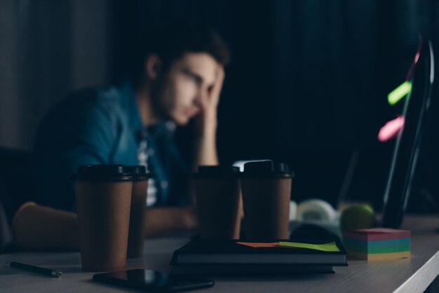 Selective focus of young programmer working at night near disposable cups