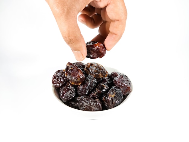 Selective focusHand holding dried sweet dates on bowl isolated on white background Healthy food concept