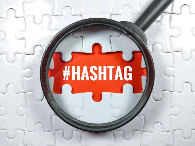 Selective focusWord HASHTAG with magnifying glass and jigsaw puzzle on red backgroundBusiness concept