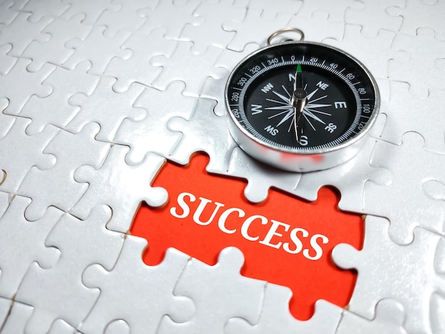 Photo selective focusword success with compass on jigsaw puzzle and red backgroundbusiness concept