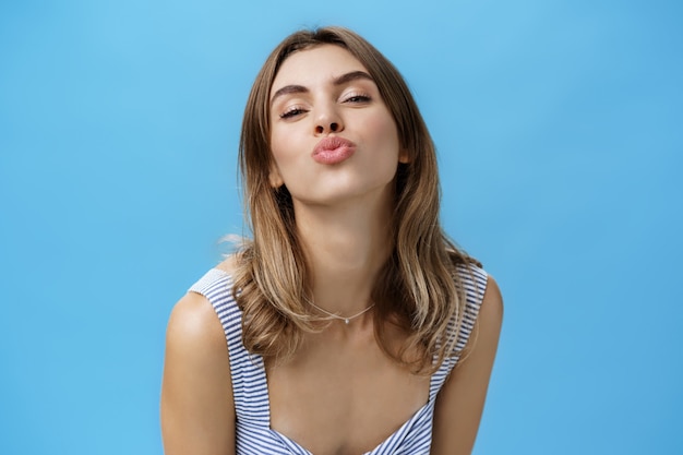 Self-assured happy and charismatic young sensual girlfriend pulling face towards camera, folding lips to give passionate kiss standing delighted and confident