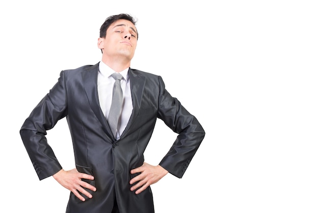 Self assured young male boss with dark hair in formal suit and tie standing against white background with hands on waist and looking at camera with confidence