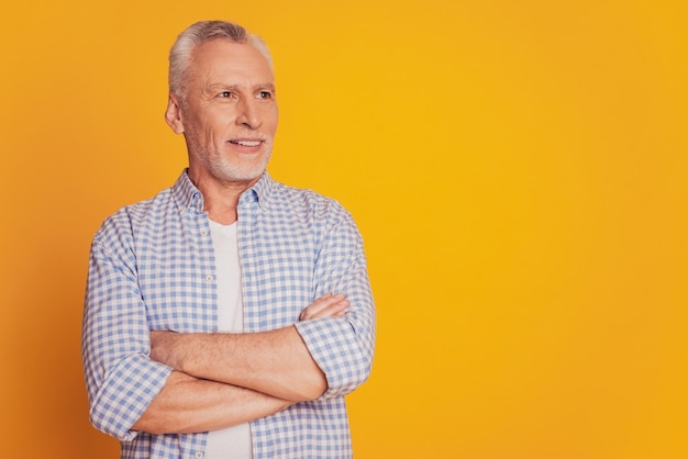 Self confident man keeps hands crossed looks at camera isolated over yellow background