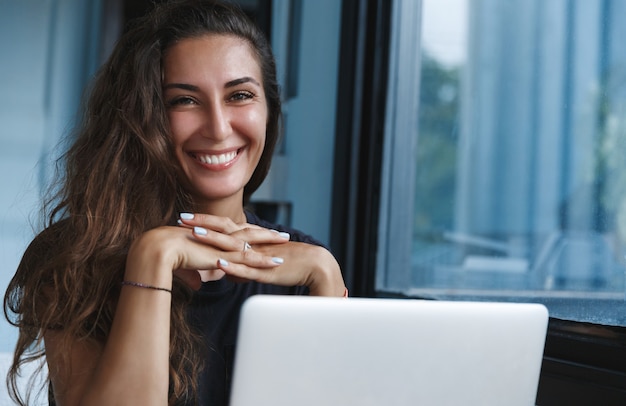 自宅で仕事をし、ノートパソコンを使用し、カメラに向かって幸せそうに笑っている自営業の成人女性。