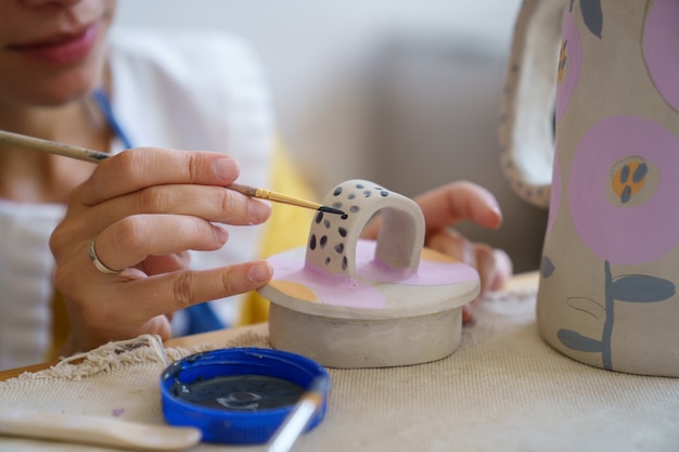 Self employed ceramist girl decorating ceramic cup for clay jug at master class in pottery studio