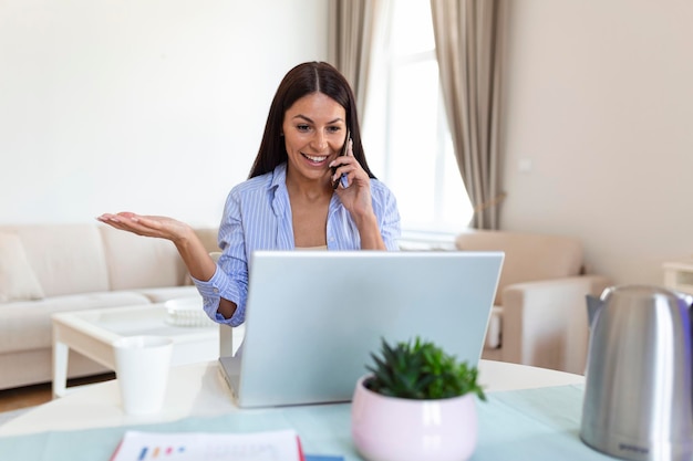 Self employed woman working with her phone and laptop at home\
happy woman using mobile phone while working at home with\
laptop