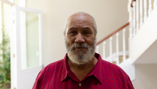 Self isolation in quarantine lock down. portrait of a senior mixed race man with grey hair and a beard at home, standing in the hallway and smiling to camera