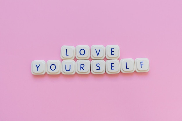 Photo self love concept illustrated with love yourself made with game letters on a pink background