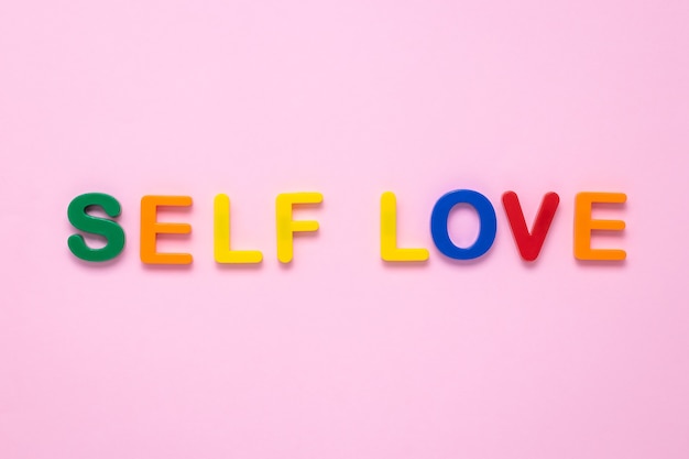 Photo self love text on pink paper background made from colorful plastic letters.