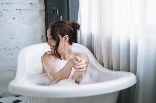 사진 자기 사랑 성인 미소 짓는 갈색 머리카락의 여자가 집에서 거품으로 목욕