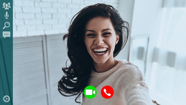 Self portrait of attractive young woman smiling and looking at\
camera while having video call