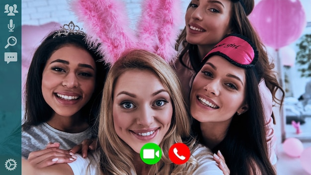 Self portrait of attractive young women in pajamas smiling and\
looking at camera while having video call