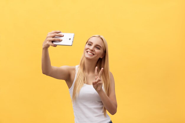 Self portrait of charming cheerful girl shooting selfie on front camera gesturing v-sign peace symbol 