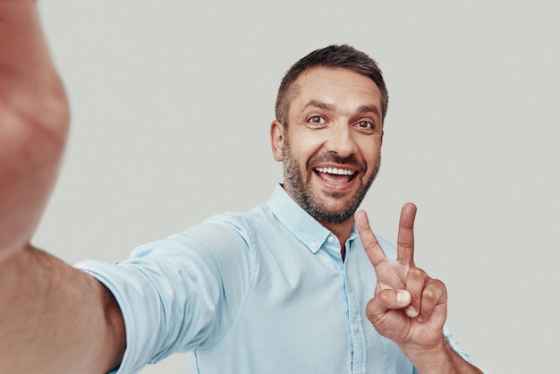 Self portrait of handsome young man looking at camera and smiling while standing against grey background