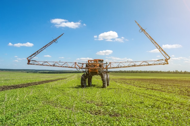 Self-propelled sprayer works on a field under a blue sky with clouds