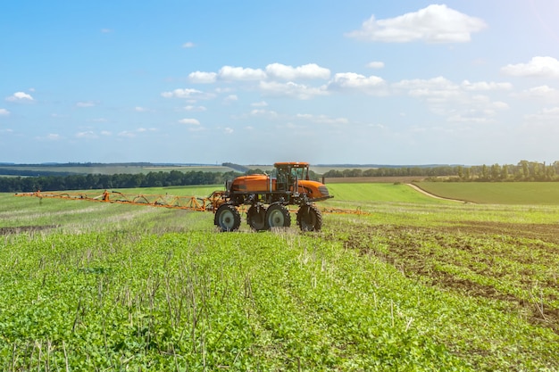 Self-propelled sprayer works on a field under a blue sky with\
clouds